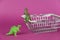 Dinosaurs and a shopping cart against a purple background. Dinosaurs next to empty shopping cart. Green plastic miniatures of
