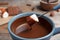 Dipping marshmallow into pot with chocolate fondue on table