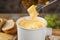 Dipping piece of cheese into tasty cheese fondue on table