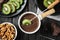 Dipping slice of kiwi into  pot with milk chocolate on black wooden table, top view