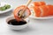 Dipping tasty sushi into soy sauce at white marble table, closeup