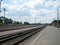 Direct railway track through a small station outside the city on a summer day. Steel rails are laid along a low platform.