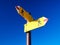 Directional marker for a mountain hike. Yellow bright sign with an arrow against the blue sky. Navigation in a hiking trip.