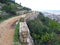 Dirt clay road uphill, vintage brickwork on side, panorama of city below, Montgo mountain