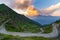 Dirt mountain road leading to high mountain pass in Italy Colle delle Finestre. Expasive view at sunset, colorful dramatic sky,