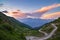Dirt mountain road leading to high mountain pass in Italy Colle delle Finestre. Expasive view at sunset, colorful dramatic sky,