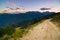 Dirt mountain road leading to high mountain pass in Italy. Expasive view at sunset, colorful dramatic sky, adventures in summer ti