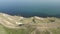 Dirt mountain road runs along hillside along sea. Man rides bike in road