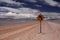 Dirt road into endlessness of Atacama desert -  yellow traffic sign showing left direction, Chile