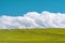 Dirt road through green field and fluffy clouds over hill. Plateau Assy, Kazakhstan