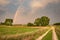 Dirt road and green field, trees and rainbow in the sky
