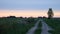 Dirt road in an open field at sunset on a summer day. The sun sheds a parting light on the sky, which turns pink. The field was