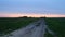 Dirt road in an open field at sunset on a summer day. The sun sheds a parting light on the sky, which turns pink. The field was