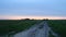 Dirt road in an open field at sunset on a summer day. The sun sheds a parting light on the sky, which turns pink. The field was