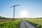 Dirt road, power line and sun symbolizing path towards renewable energy