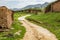 Dirt road winds up a small hill around a mud wall in rural China with a power line running across the top