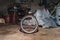 Dirty Bicycle Wheel on the Floor of a Messy Home Garage with Equipment, Workbench, Tools and Cloth in Background