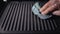 Dirty electric grill. Male hand wiping with cloth grill. Cleaning electric grill dirty plate with rag, detail on man