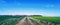 Dirty farm road with wide blue sky and green fields