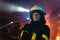 Dirty female firefighter looking at camera with fire truck at background at night.