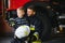 Dirty firefighter in uniform holding little saved boy standing on black background.