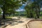 A dirty footpath in the park with a park bench surrounded by lush green trees reflecting off the water of the Chattahoochee river