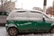 Dirty green compact car in the snow can not go. The first snowfall. cars covered in snow in the city. Transport problems, poorly