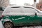 Dirty green compact car in the snow can not go. The first snowfall. cars covered in snow in the city. Transport problems, poorly