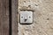 Dirty grey old small broken light switch next to wooden doors on dilapidated wall of abandoned family house ruins