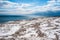 Dirty ice field near water under partly cloudy blue sky.