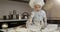 A dirty little cook plays with flour and dough on the table in the kitchen.