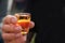 Dirty mens hand holding a shot glass with orange alcohol drink,