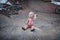 Dirty plastic baby doll sitting on the ground in front of a metal shop waving