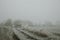 Dirty road and straw bales in the distance in tall grass next to the field during the freezing foggy