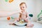 Dirty and smiling baby on a white table being fed by his mother`s hand, while laughing while trying the blw method