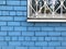 dirty white window with a grille against the background of a blue brick wall.