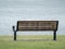 Dirty wooden and metal park bench on grass looking at water