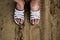 Dirty, working and tired girl`s feet in white dusty Slippers on the background of sand.