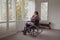 Disabled active senior man looking through window on wheelchair in a comfortable home