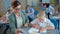 Disabled boy with down syndrome studys shapes with teacher sitting at desk on background of classmates during the lesson