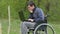 Disabled man thinks problems wheelchair with a laptop in a wheelchair working on green background nature