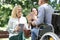 Disabled man in wheelchair giving english textbook to his female friends in park