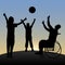 A disabled man in a wheelchair plays ball with a child and a woman at dawn.