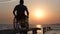 Disabled man on wheelchair resting to sea pier on background of orange sky and water at sunset