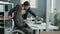 Disabled office worker in wheelchair talking to male colleague looking at laptop screen