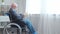 Disabled old man is sitting in a wheelchair at home alone. A handicapped person in a wheelchair is reading the book