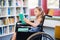 Disabled school girl reading book in library