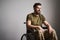 Disabled soldier sitting in a wheelchair and smiling on gray background