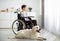 Disabled teen boy in wheelchair with his dog looking out window at home. Human animal friendship concept