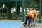 Disabled teenage boy in wheelchair with basketball ball at outdoor court